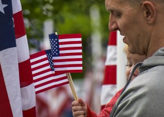 A man and child holding American flags during a patriotic outdoor event.